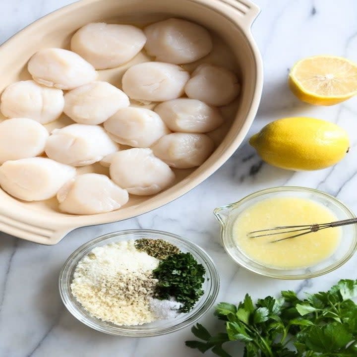 Sliced lemon, melted butter, salt, pepper, and raw scallops in bowls.