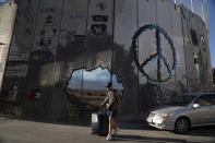 A foreign tourist passes Israel's controversial separation barrier as he arrives to check in any the Walled Off Hotel in the West Bank town of Bethlehem, Sunday, June 19, 2022. Despite the roaring return of travelers, challenges and uncertainty cast shadows over the post-pandemic landscape. Full recoveries are generally not expected until at least 2024. (AP Photo/Maya Alleruzzo)