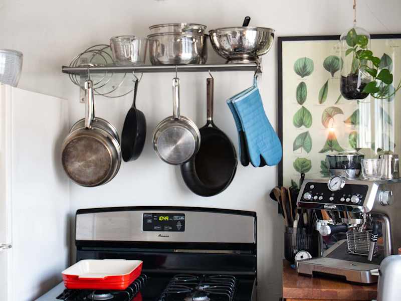 Black stove with pots and pans, oven mitts hanging above on shelf/rack. Espresso machine and toaster on counter to the right