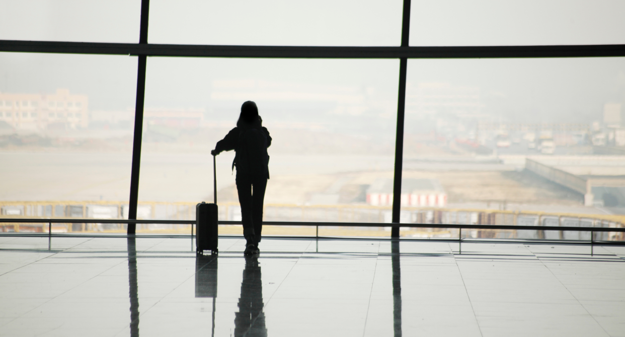 person standing in airport looking out window with suitcase, amazon suitcase luggage set on sale