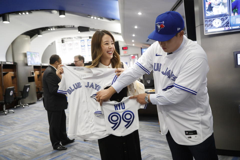 Toronto Blue Jays newly signed pitcher Hyun-Jin Ryu, right, holds up a jersey for his expected baby alongside his wife Ji-Hyun Bae following a news conference announcing his signing to the team in Toronto, Friday, Dec. 27, 2019. (Cole Burston/The Canadian Press via AP)