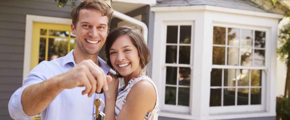 Couple With Keys Standing Outside New Home