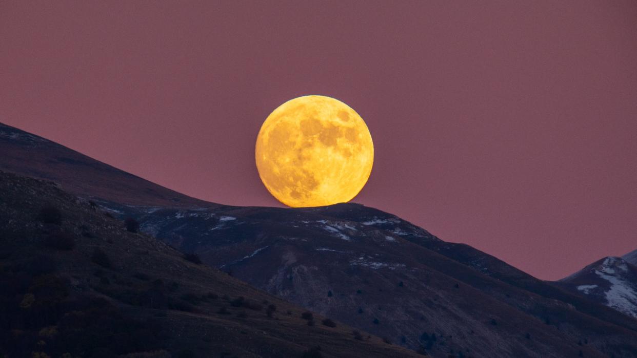  A large full moon rises over a mountain range. 