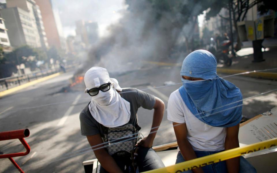 Anti-government demonstrators rest behind a barricade in Caracas - Credit: AP