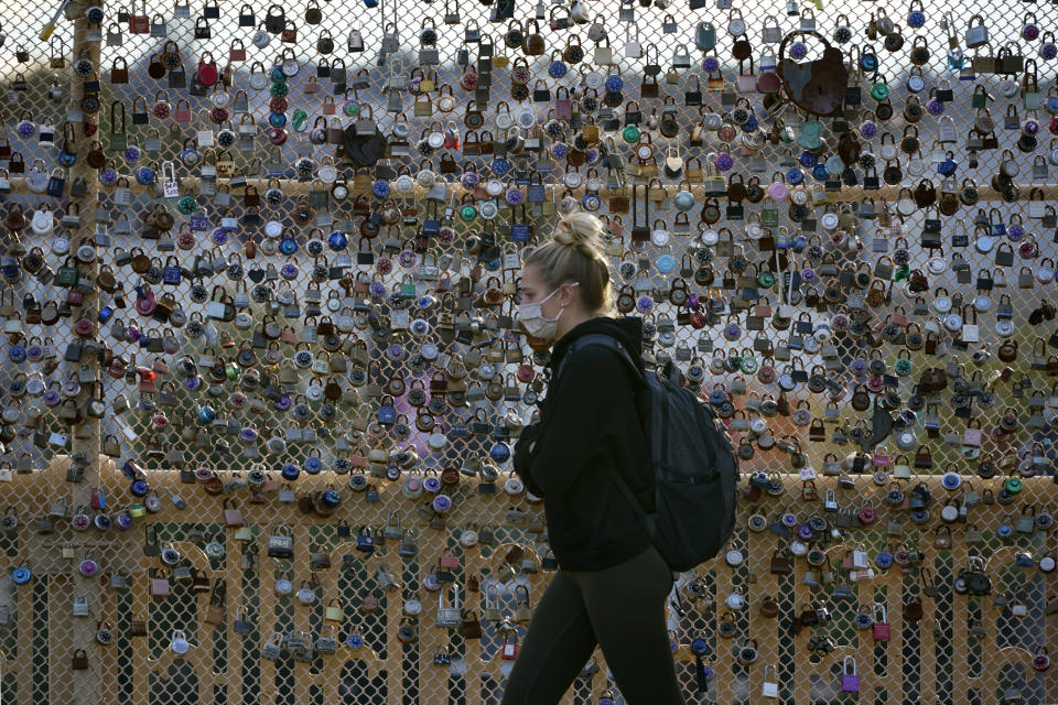 FILE - Locks cover the fence on the Love Bridge in the Oakland neighborhood of Pittsburgh as a person walks by Nov. 3, 2021. A poll from MTV Entertainment Group and The Associated Press-NORC Center for Public Affairs Research finds that Americans ages 13 through 56 think the pandemic made parts of their lives harder, but Gen Z reported higher levels of disruption to their education and dating lives. (AP Photo/Gene J. Puskar, File)