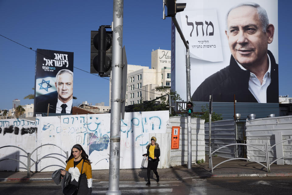 People walk next to election campaign billboards for Likud Party, shows Israeli Prime Minister Benjamin Netanyahu, right, and the Blue and White party, the opposition party led by Benny Gantz, left, in Bnei Brak, Israel, Sunday, March. 1, 2020. Israel heads into its third election in less than a year on Monday, March 2nd. (AP Photo/Oded Balilty)