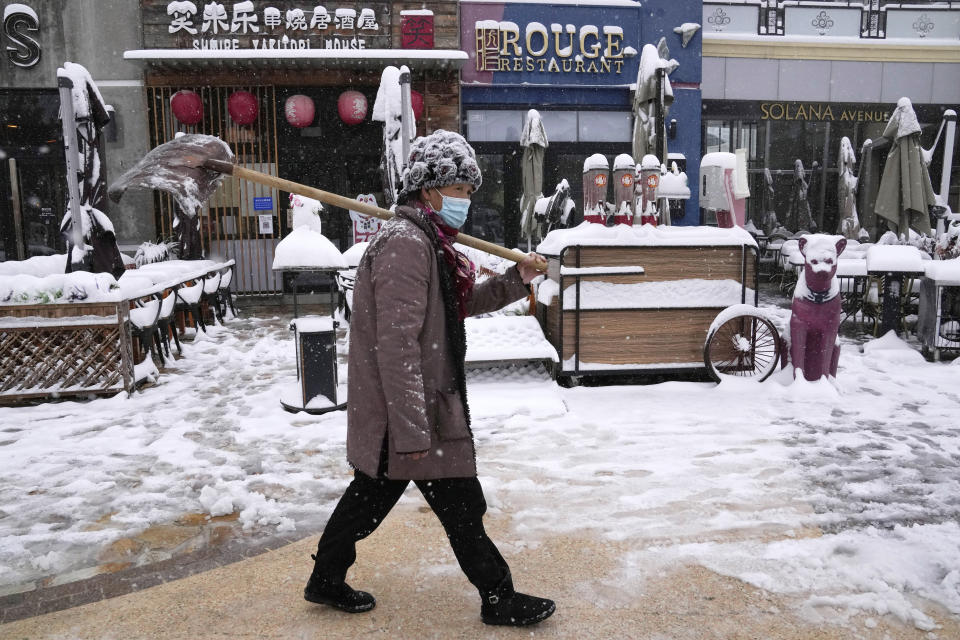 A worker walks with a shovel past restaurants at a mall in Beijing, China, Sunday, Nov. 7, 2021. An early-season snowstorm has blanketed much of northern China including the capital Beijing, prompting road closures and flight cancellations. (AP Photo/Ng Han Guan)