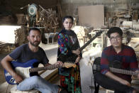 In this Thursday, July 26, 2018, photo, Afghan musicians Mohammad Rezai, right, Hakim Ebrahimi, left, and Soraya Hosseini, members of the Arikayn rock band, pose for a photo at a furniture workshop in Pakdasht, outside Tehran, Iran. The band, made up of Afghan migrants, plays Metallica-inspired ballads about the struggles of millions of Afghans who have fled to Iran to escape decades of war and unrest. (AP Photo/Ebrahim Noroozi)