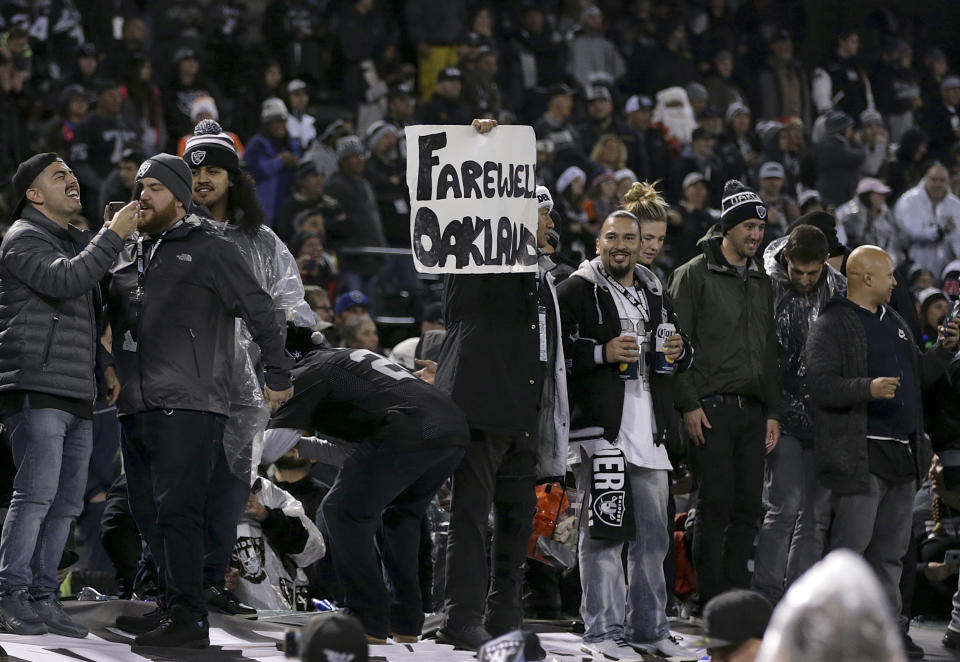A fan holds up a sign while standing on a dugout at Oakland-Alameda County Coliseum after the final Raiders game at the stadium. (AP)