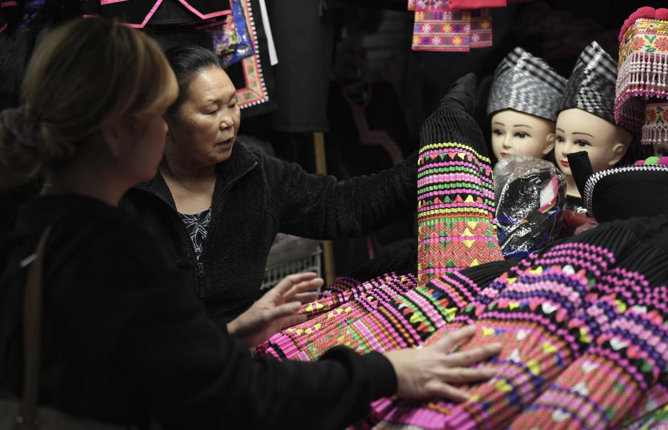 Shoppers look for pleated skirts and other clothing for Hmong New Year for sale at the stall of Elisa Her, left, in the Hmong Village covered market in St. Paul, Minn., on Thursday, Nov. 16, 2023. The New Year, celebrated at various dates during fall by Hmong Americans, is the most important traditional spiritual celebration for these Southeast Asian refugees who settled in the United States after fighting on its side in the Vietnam War. (AP Photo/Mark Vancleave)