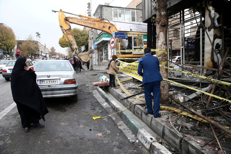 FILE PHOTO: A woman looks on as people hang a banner outside a burnt bank, after protests against increased fuel prices, in Tehran