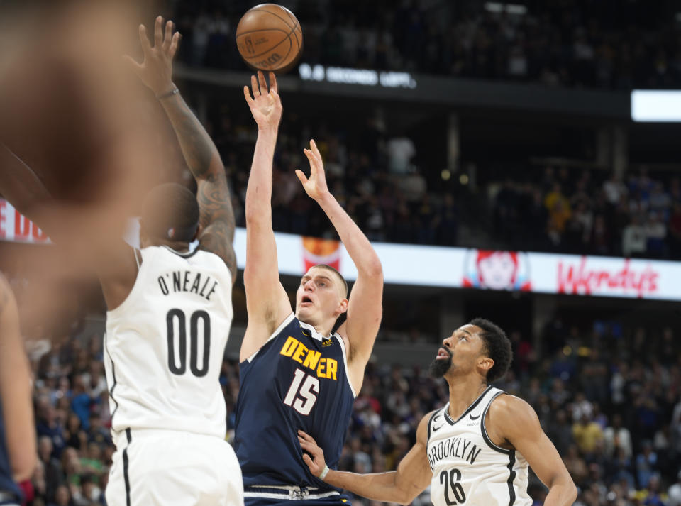 Denver Nuggets center Nikola Jokic hoists up a shot between Brooklyn Nets forward Royce O'Neale, left, and guard Spencer Dinwiddie late in the second half of an NBA basketball game, Sunday, March 12, 2023, in Denver. (AP Photo/David Zalubowski)