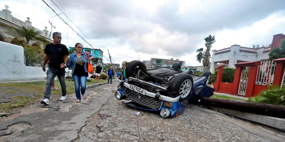 AME4766. LA HABANA (CUBA), 28/01/2019.- Vecinos caminan junto a un carro volcado tras el paso de un tornado, este lunes, en La Habana (Cuba). Al menos tres personas han muerto y 172 han resultado heridas por un tornado que azotó esta madrugada la barriada de Regla, en La Habana, informó hoy el presidente de Cuba, Miguel Díaz-Canel. EFE/Ernesto Mastrascusa