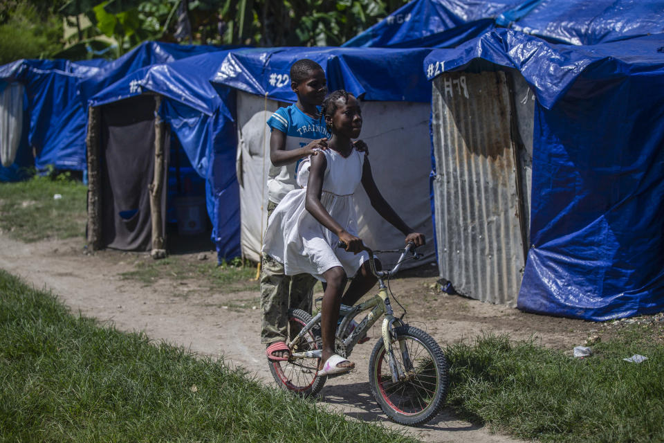 Children cycle through Camp Devirel set up by people left homeless by last year’s 7.2-magnitude earthquake, in Les Cayes, Haiti, Wednesday, Aug. 17, 2022. UNICEF has warned that more than 250,000 children still have no access to adequate schools and that the majority of 1,250 schools destroyed or damaged have not been rebuilt. (AP Photo/Odelyn Joseph)