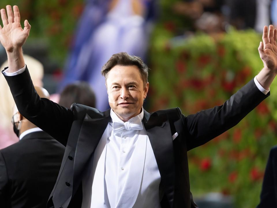 Elon Musk greets onlookers with both hands waving, at the 2022 Met Gala