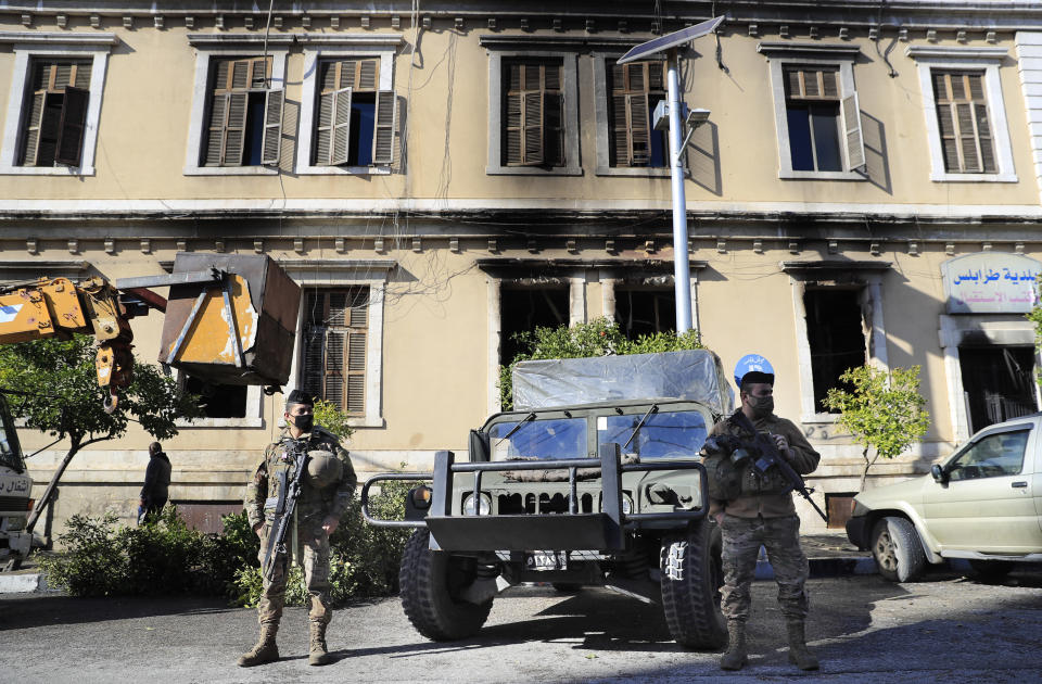 Lebanese army soldiers stand guard outside the building of Tripoli municipality that was set on fire by protesters Thursday night, during a protest against deteriorating living conditions and strict coronavirus lockdown measures, in Tripoli, Lebanon, Friday, Jan. 29, 2021. A cautious calm prevailed in the northern city hours after rioters set fire to several buildings, capping days of violent clashes as anger over growing poverty made worse by the coronavirus lockdown boiled over.(AP Photo/Hussein Malla)