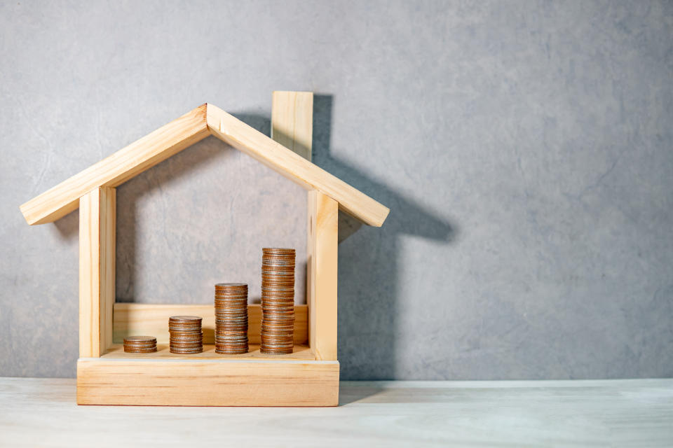 Coins stacked in wooden house frame on table. Home mortgage loan rate. Saving money for future retirement. Real estate investment or property ladder concept. Housing project for construction business