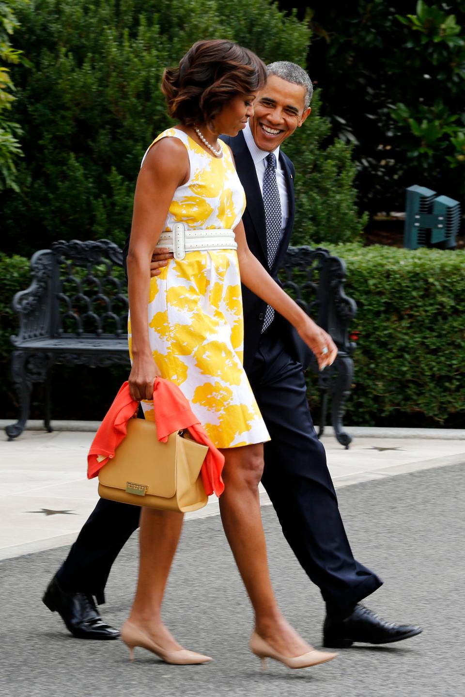 michelle obama wearing yellow floral dress while barack obama walks alongside her smiling