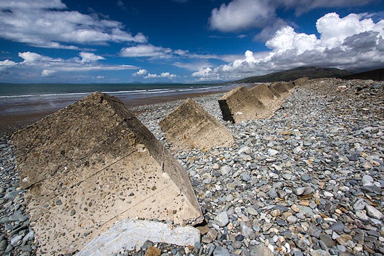 A series of concrete cubes line a pebble beach.