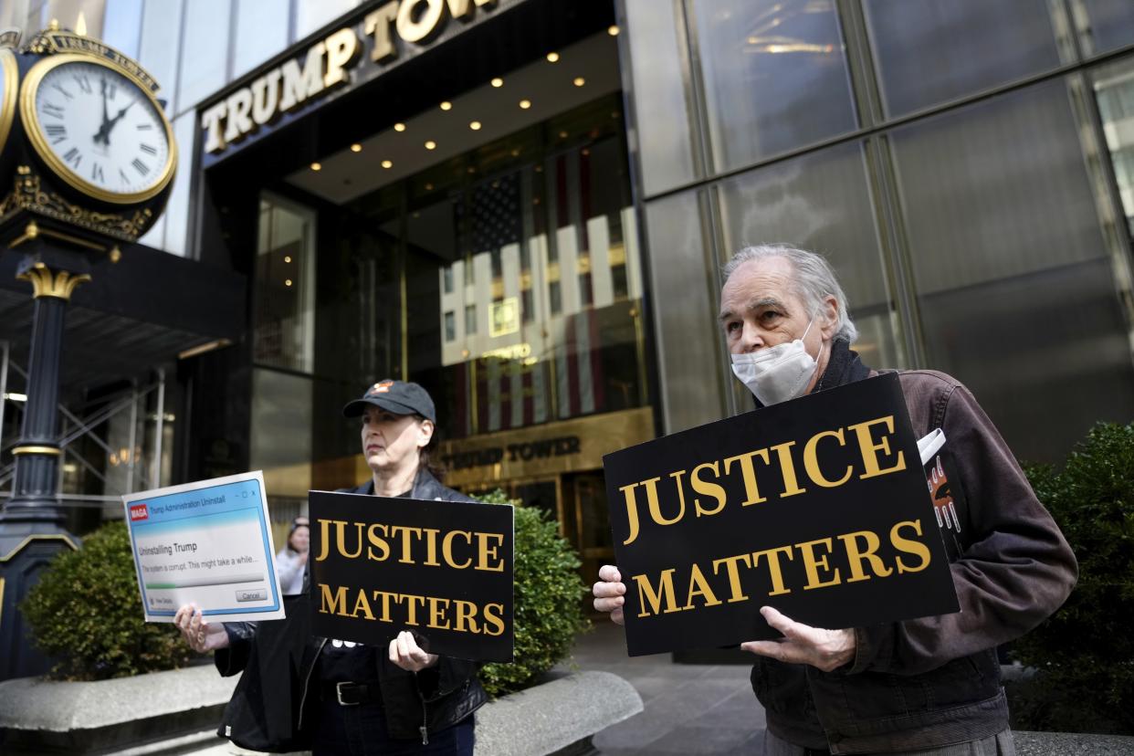 Kathleen Zea, left, and Daniel Olsen, right, hold signs protesting former President Donal Trump, outside Trump Tower on Wednesday, March 22, 2023, in New York. (AP Photo/Bryan Woolston)