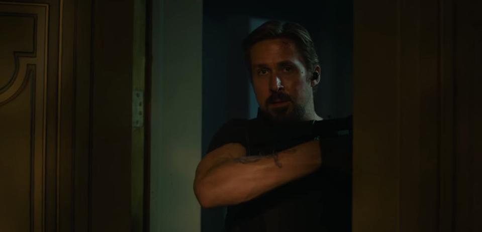 Six holding a gun and looking through a doorway in "The Gray Man"