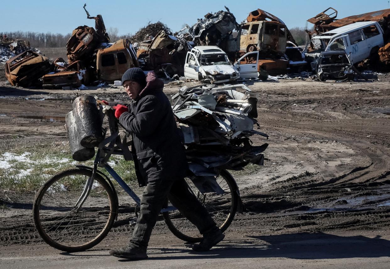 A local resident carries a collected scrap metal on a bicycle near civilian cars and military vehicle destroyed amid Russia's attack on Ukraine, are seen in the town of Bucha, before the first anniversary of its liberation, outside Kyiv, (REUTERS)
