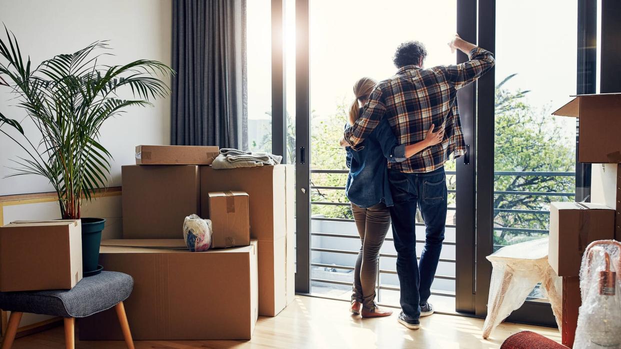 relaxed middle aged couple holding each other while looking out on their balcony together at their new home.