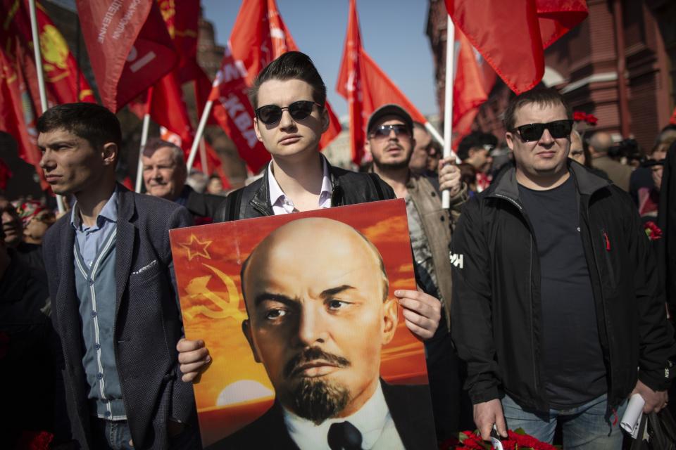 FILE - Russian Communists and supporters walk with their flags and a portrait of Vladimir Lenin, the founder of the Soviet Union, to visit his mausoleum in Red Square in Moscow, Russia, to mark the 149th anniversary of his birth, on Monday, April 22, 2019. On the 100th anniversary of his 1924 death, Lenin is mostly an afterthought in modern Russia. (AP Photo/Alexander Zemlianichenko, File)