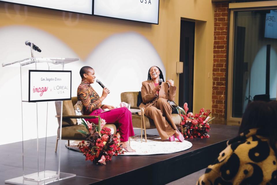 Two black women laughing and speaking into microphones as they sit onstage