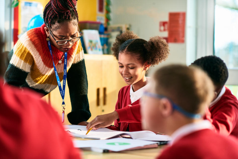 Teacher assists student with schoolwork among peers in classroom setting