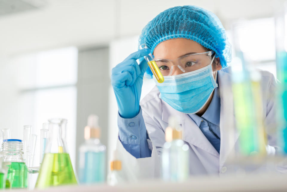 Lab worker holding a vial containing a yellow liquid.