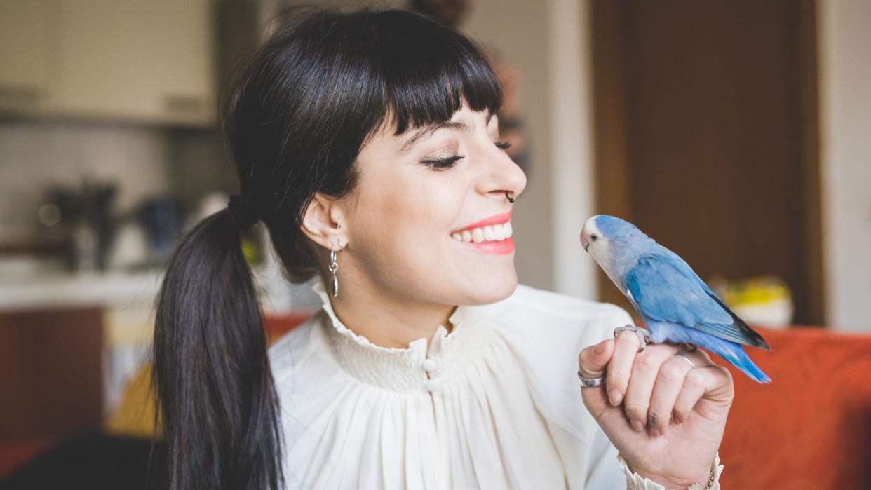  Woman smiles at pet bird. 