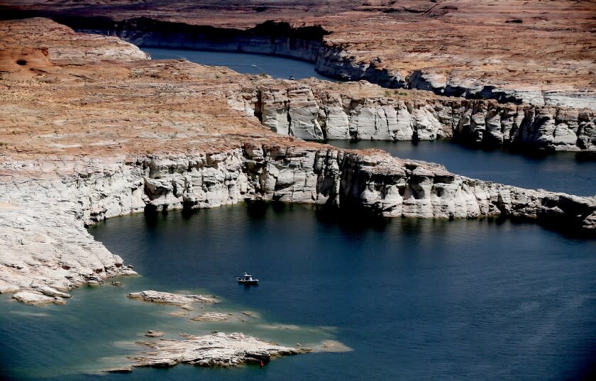 LAKE POWELL, UT. - DEC 24, 2021. A boat floats on Lake Powell, a vast reservoir of Colorado River water situated near the Utah-Arizona border. A white "bathtub ring" on the lake's shores show how much water levels have dropped during a decade of severe drought. (Luis Sinco / Los Angeles Times)