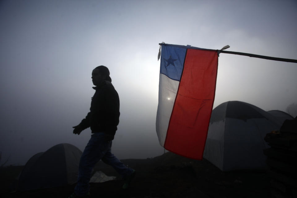 A man walks past a Chilean flag next to tents set up by people whose homes were destroyed by wildfires that burned through urban areas of the city of Valparaiso, Chile, Tuesday Apr. 15, 2014. A raging fire leaped from hilltop to hilltop in this port city, killing dozens of people and destroying thousands of homes. (AP Photo/Luis Hidalgo)