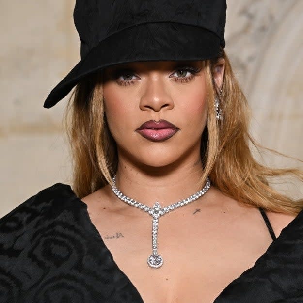 Close-up of Rihanna wearing a black hat and a diamond necklace, serious expression