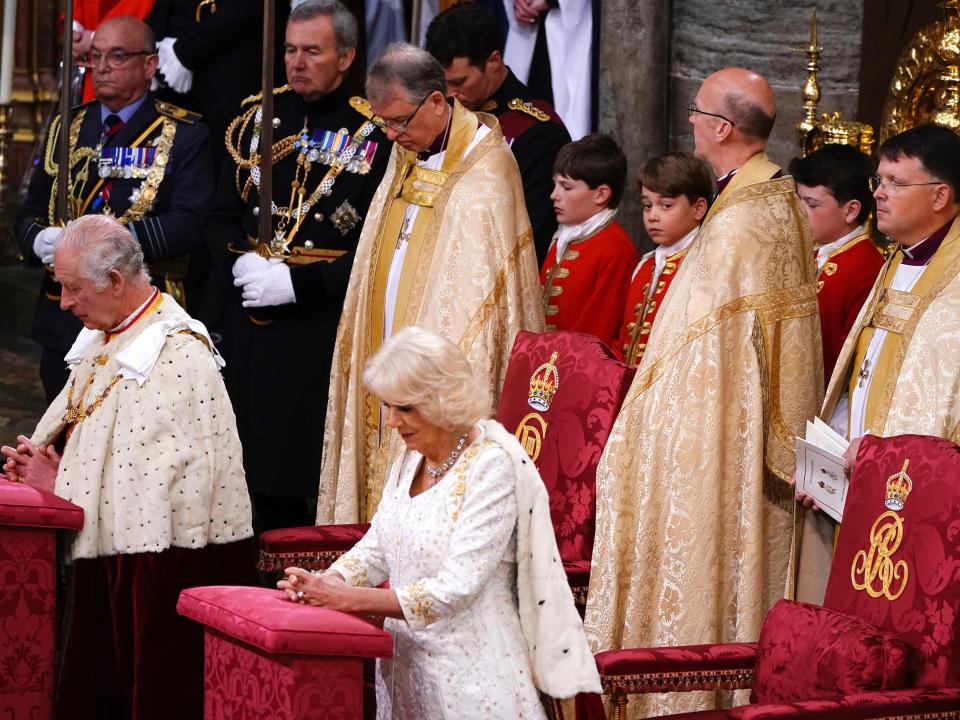 Charles and Camilla stand with hands folded as Prince George stands behind them