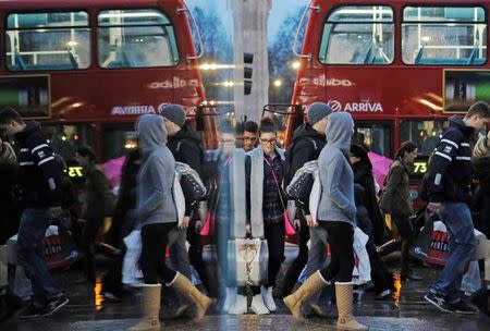 Shoppers are reflected in a shop window as they walk along Oxford Street on the last Saturday before Christmas, in London December 21, 2013. REUTERS/Luke MacGregor/File Photo