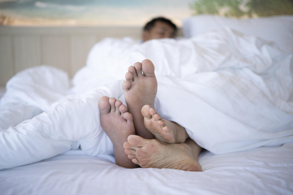 A couple lays in bed together with their feet touching