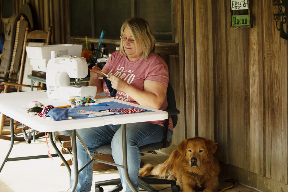 In this April 11, 2020, photo, Cathia Schmarje sews a face mask on the front porch of her home in Liberty County, Florida. She's sewn masks for her son and his employees, and she'll give some to townsfolk who need one. For weeks, there had been chatter across Liberty County in Florida’s Panhandle about how the coronavirus could devastate the 8,300 people who live there. As the coronavirus spread across Florida, Liberty became the last county without a case. (AP Photo/Bobby Caina Calvan)