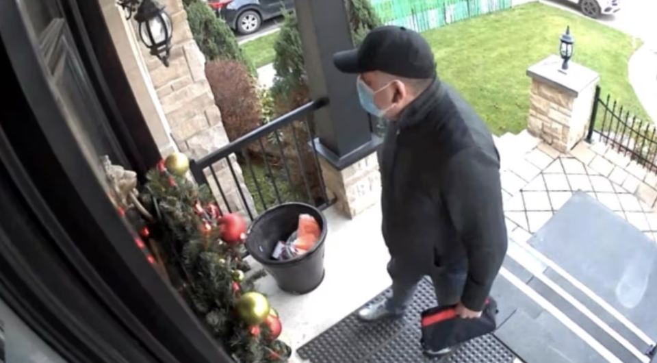 A surveillance camera image shows the Facebook Marketplace buyer waiting for Mattel to open the door. Only his eyes are visible under the baseball hat and above the mask on his face. He clutches the black pouch containing $15,000. (Submitted by Laurent Mattel)