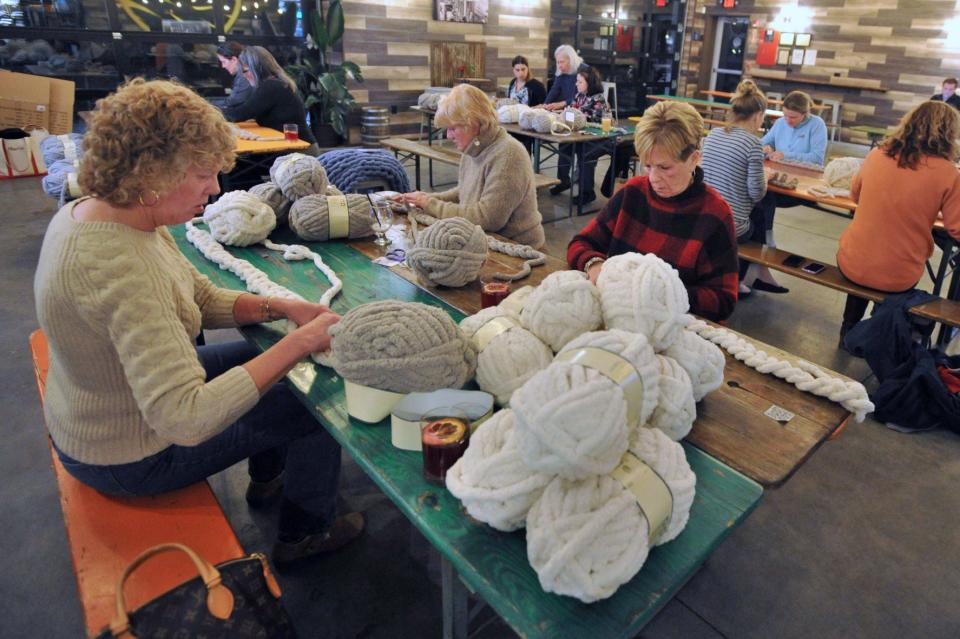 Skeins of yarn are piled on a table as knitters, from left, Theresa Harkin, Ursula Ceurvels and Cathy Joyce, all of Weymouth, create blankets during the Chunky Knit Blanket Party at Vitamin Sea Brewing in Weymouth, Tuesday, Feb. 21, 2023.