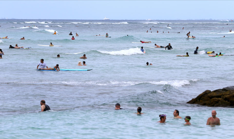 People swim and surf off Waikiki Beach in Honolulu, Tuesday, Aug. 24, 2021. Hawaii was once seen as a beacon of safety during the pandemic because of stringent travel and quarantine restrictions and overall vaccine acceptance that made it one of the most inoculated states in the country. But the highly contagious delta variant exploited weaknesses as residents let down their guard and attended family gatherings after months of restrictions and vaccine hesitancy lingered in some Hawaiian communities.(AP Photo/Caleb Jones)