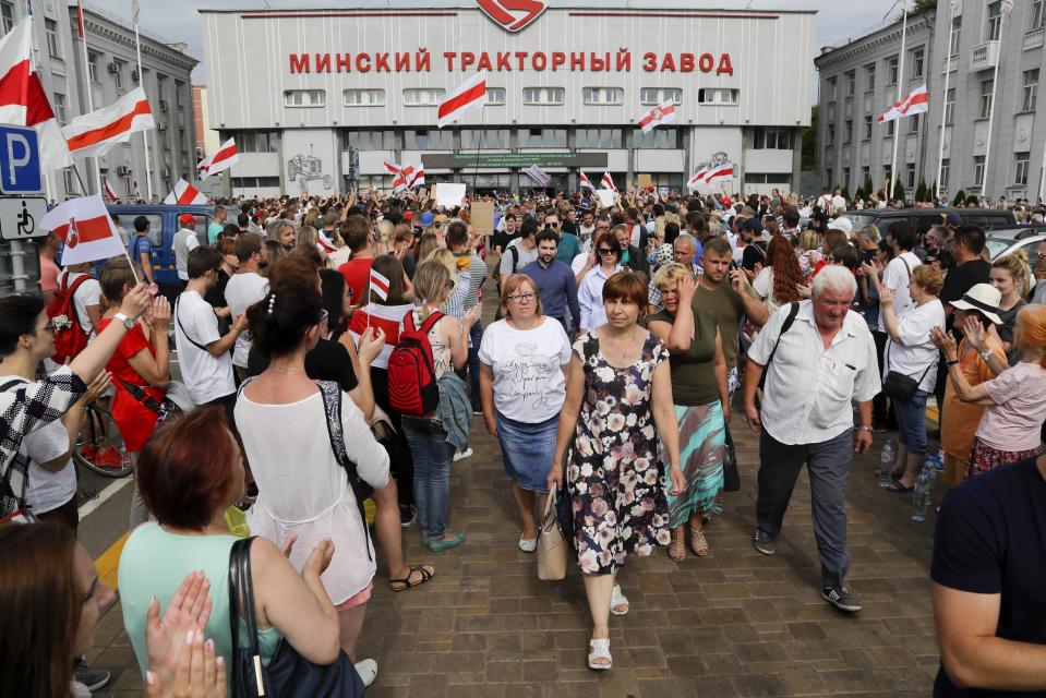 Workers of the Minsk Tractor Works Plant leave the plant after their work shift as activists with old Belarusian national flags greet them in Minsk, Belarus, Tuesday, Aug. 18, 2020. Workers in Belarus are joining a growing strike, turning up pressure on the country's authoritarian leader to step down after winning an election they say was rigged. (AP Photo/Sergei Grits)
