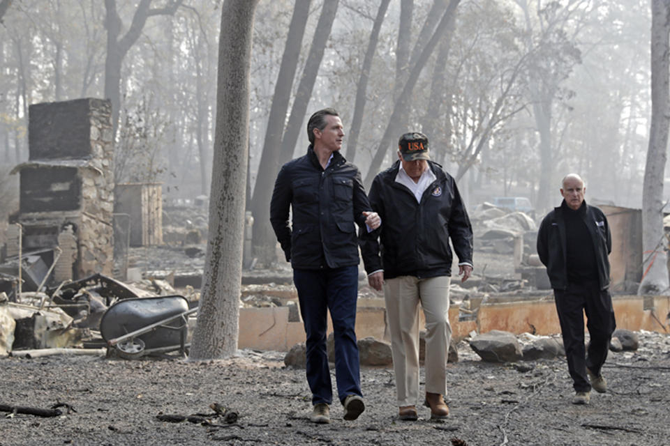 FILE - In this Nov. 17, 2018 file photo, President Donald Trump talks with California Gov.-elect Gavin Newsom, left, as California Gov. Jerry Brown, walks at right during a visit to a neighborhood destroyed by the Camp wildfire in Paradise, Calif. Newsom is declaring a state of emergency to speed up forest management ahead of the next wildfire season and will sign an order Friday, March 22, 2019, allowing fire officials to bypass certain environmental and other regulations in order to clear dead trees and vegetation more quickly. It will apply to 35 projects across 90,000 acres of land. (AP Photo/Evan Vucci, File)