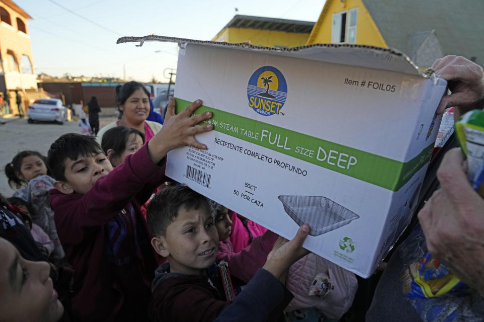 Migrant children hold a box filled with food and clothes outside a shelter Wednesday, Dec. 21, 2022, in Tijuana, Mexico. Thousands of migrants gathered along the Mexican side of the southern border Wednesday, camping outside or packing into shelters as they waited for the U.S. Supreme Court to decide whether and when to lift pandemic-era restrictions that have prevented many from seeking asylum. (AP Photo/Marcio Jose Sanchez)