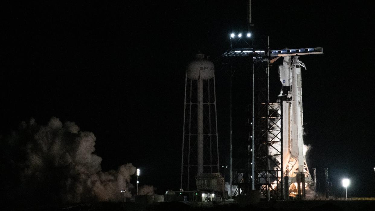  rocket at right firing its engines with smoke pouring at left. the image is taken at night  