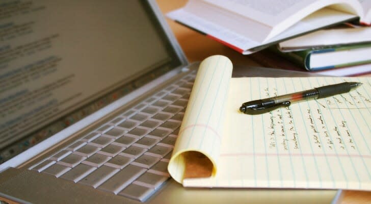 Image shows a laptop as well as a notepad with research notes written on it. Thorough research is important to complete when hiring a financial advisor.