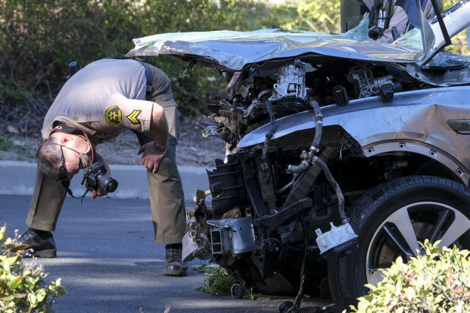 A law enforcement officer looks over a damaged vehicle following a rollover accident involving golfer Tiger Woods, Tuesday, Feb. 23, 2021, in the Rancho Palos Verdes suburb of Los Angeles. Woods suffered leg injuries in the one-car accident and was undergoing surgery, authorities and his manager said. (AP Photo/Ringo H.W. Chiu)