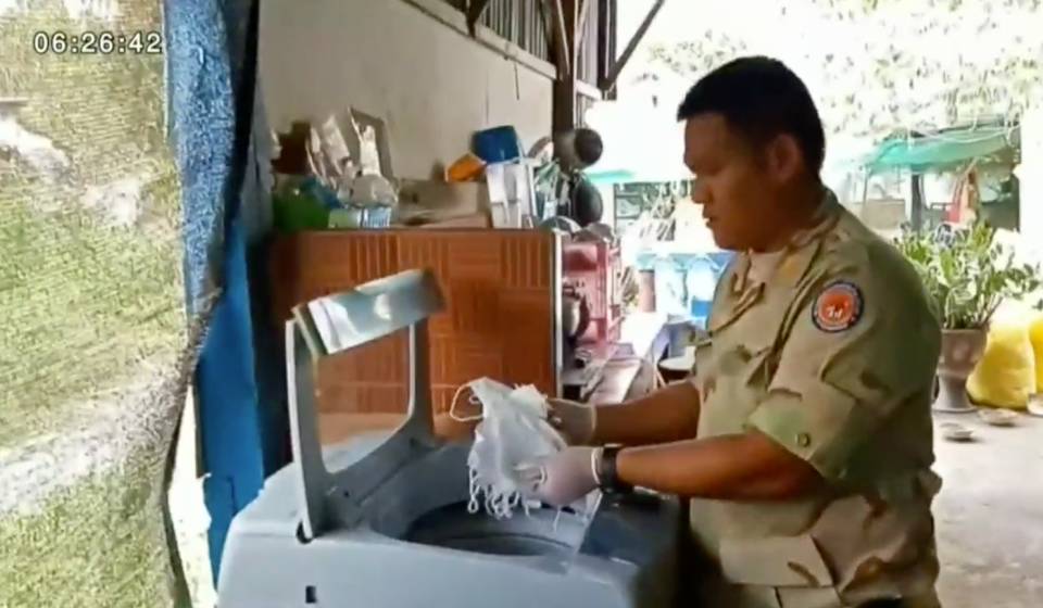 A Thai police officer pulls a handful of masks from a washing machine.