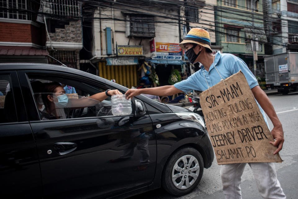A jeepney driver wearing a face mask and a placard reading "sir/mam, asking for help, we are jeepney drivers" receives alms from a motorist on a road in Manila on August 6, 2020. (Photo: LISA MARIE DAVID/AFP via Getty Images)